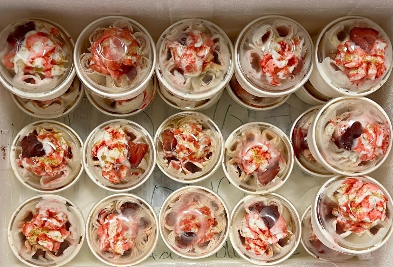 Rows of rolled ice cream cups topped with strawberries, packed for a catering order